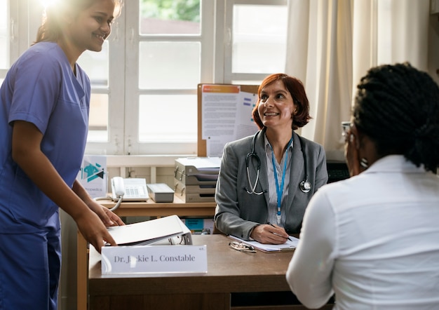A healthcare worker helping a patient fill out insurance enrollment forms at a desk in a community health center. The atmosphere should be supportive and informative.