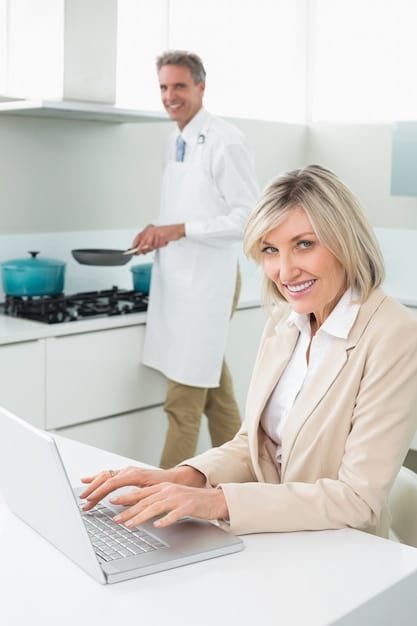 A doctor conducting a telehealth consultation with an employee, both smiling and looking at a laptop screen. The background is a clean and modern home office setup.