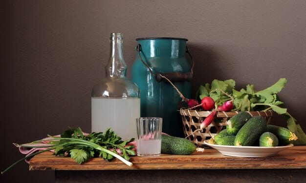A diverse array of fresh, colorful vegetables and fruits arranged artfully on a wooden table, emphasizing variety and natural goodness. There's a glass of water nearby to suggest hydration.