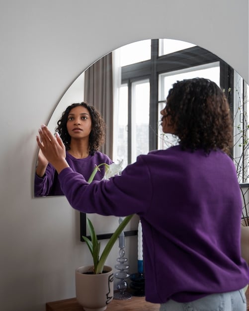A person looking thoughtfully at their reflection in a mirror, showing self-acceptance and gentle understanding, representing self-compassion and inner strength.