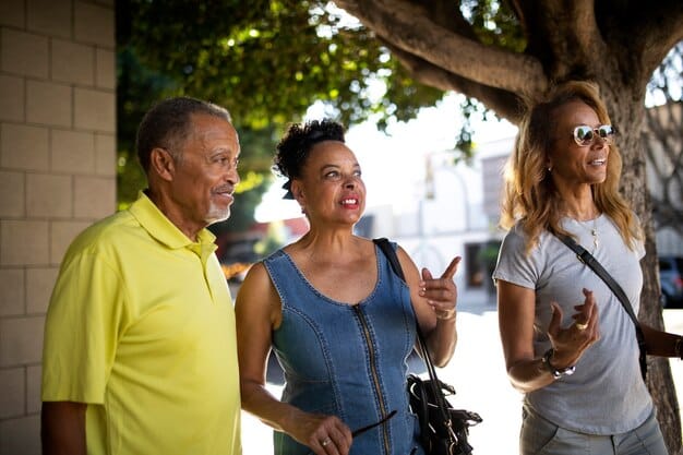 A diverse group of people of varying ages enjoying a leisurely walk together through a sun-dappled park, smiling and chatting.