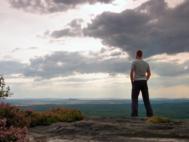 A person standing confidently on a mountain peak, overlooking a vast landscape, symbolizing overcoming challenges and achieving goals through resilience and inner strength.