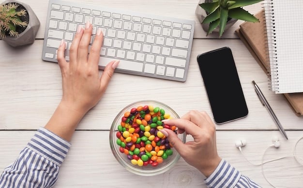 A person's hand reaching for a piece of fruit from a fruit bowl on a desk, next to a laptop, illustrating mindful and healthy snacking during work.