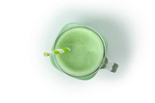 A top-down view of a vibrant green smoothie being poured into a glass, featuring ingredients like spinach, kale, banana, and a sprinkle of chia seeds, set against a background of fresh fruits and vegetables.
