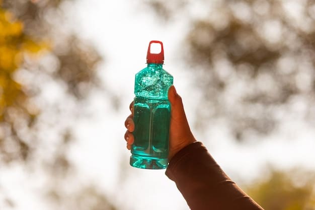 A person holding a reusable water bottle filled with fresh, clear water, with a blurred background showing an outdoor fitness setting - suggesting hydration during exercise for optimal health and energy levels. Focus is on the water bottle and the person's hand.