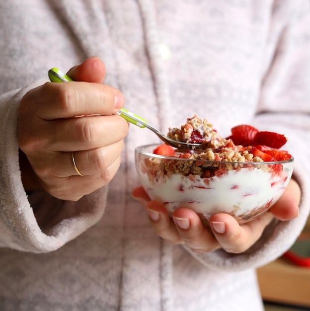 Close-up of a person eating a bowl of yogurt with berries and nuts. The image highlights the importance of gut health and probiotics for mental well-being, emphasizing The Link Between Diet and Mental Health: What You Eat Can Affect Your Mood and Well-being